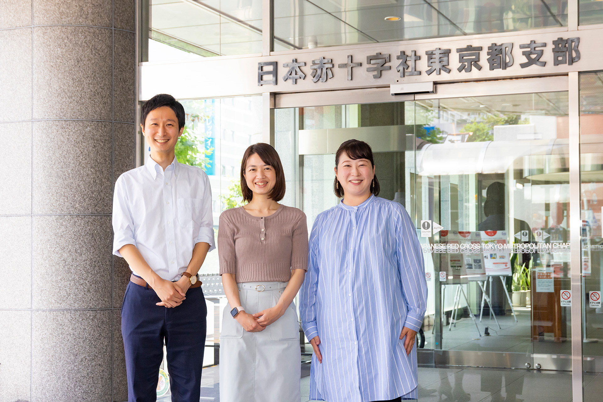 日本赤十字社東京都支部のエントランス前の高橋さん、竹松さん、笠井さん