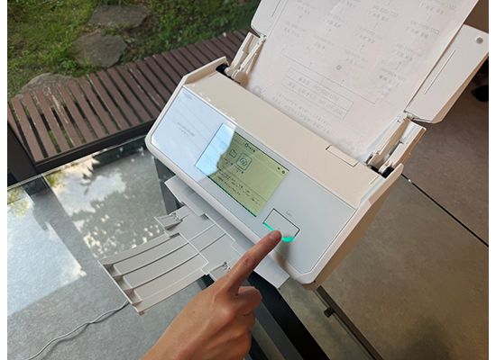 ScanSnap iX2500に紙をセットし、Scanボタンを押すところ